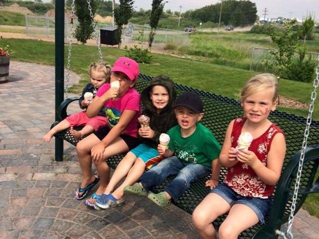 Children sitting on a swing eating ice cream.