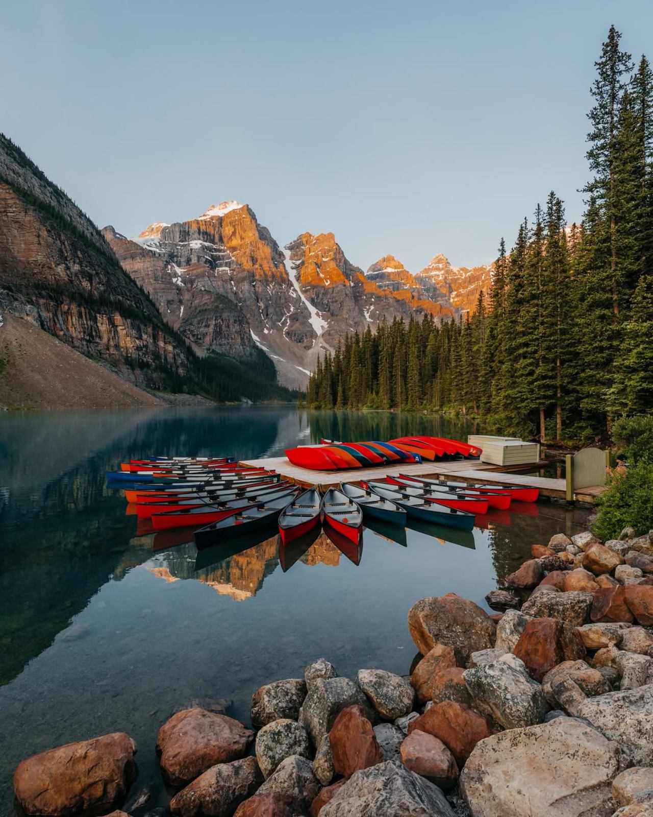 Red canoes on Moraine Lake with mountain and forest reflections in calm water.