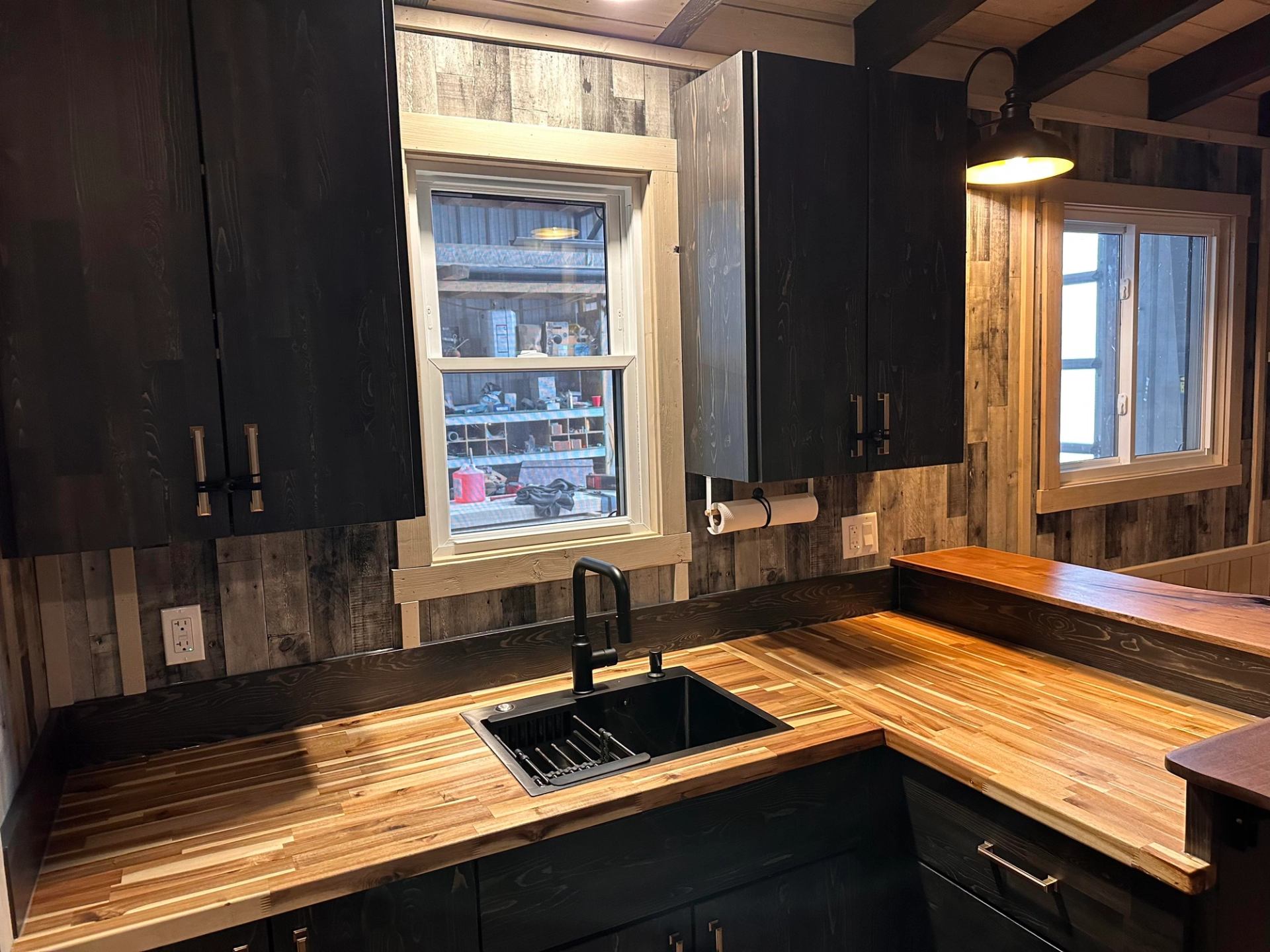 Rustic kitchen with wood countertops, black cabinets, sink and two windows.
