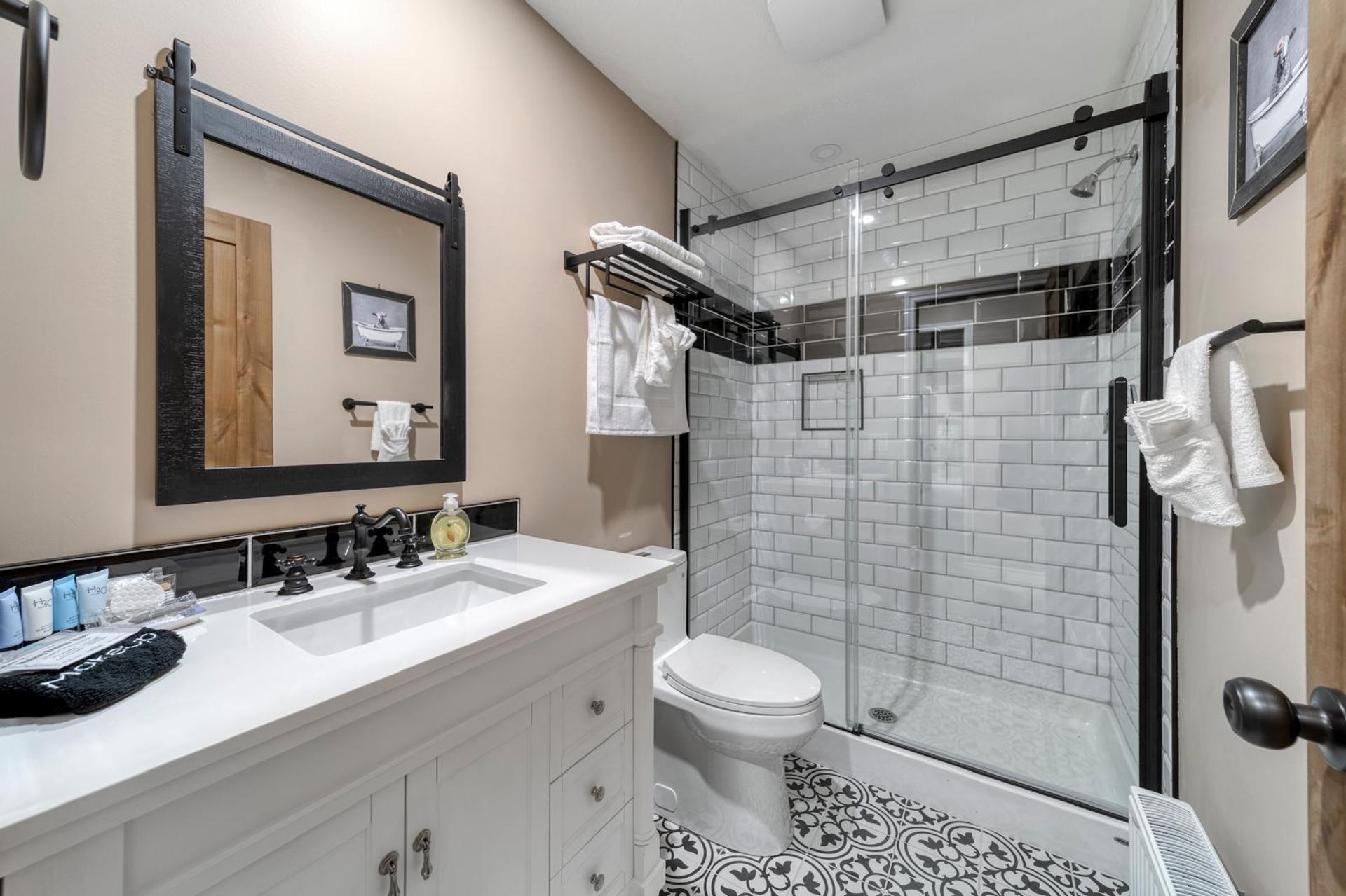Bathroom with white vanity, patterned tile floor, glass shower and folded white towels.