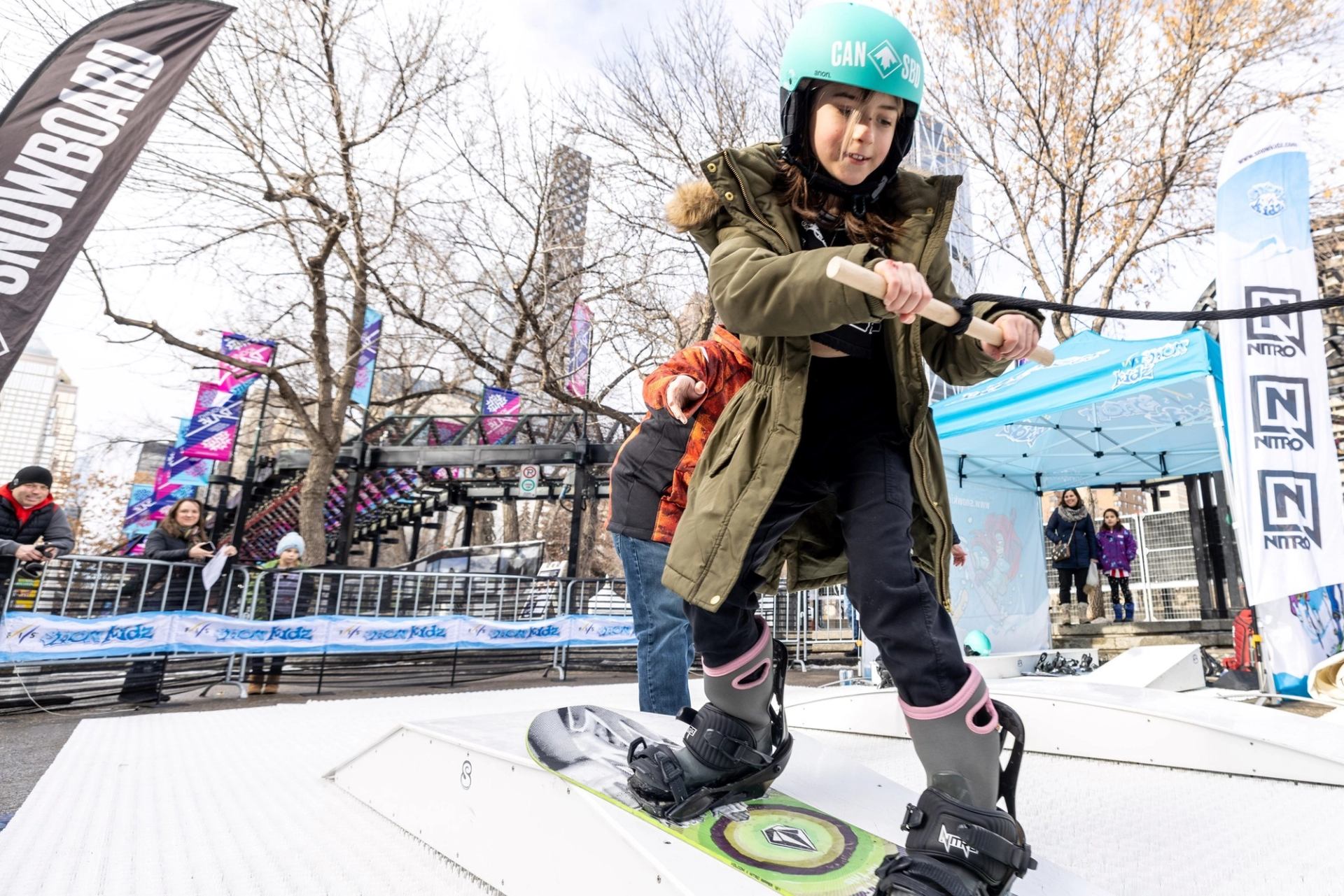 Child tries snowboarding at winter event demo station.