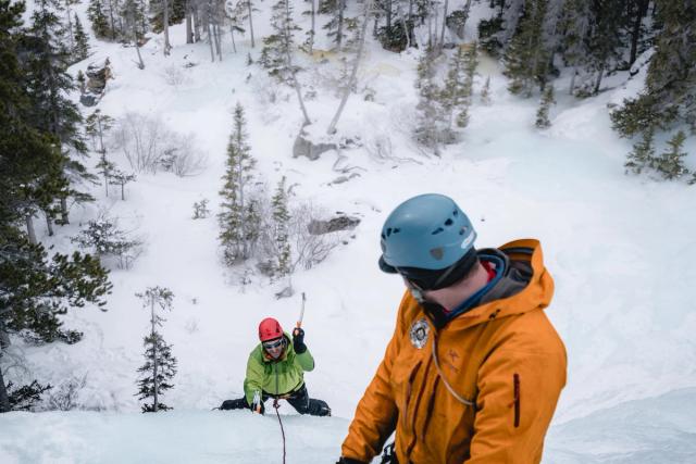 Guide looking down at an ice-climber while ice climbing in Tangle Falls in Jasper National Park