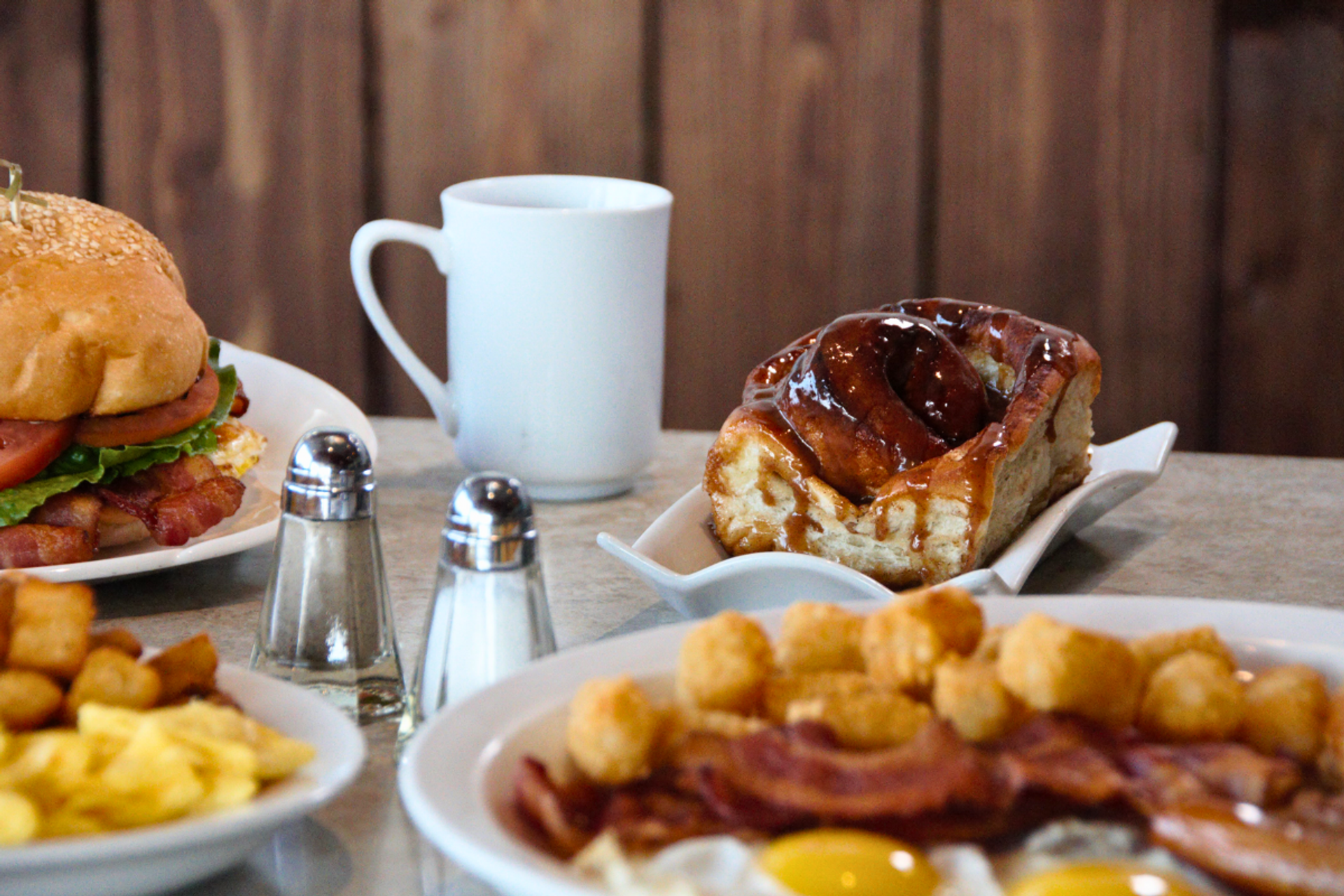 Breakfast spread with eggs, bacon, tater tots, sandwich, pastry, and coffee at Grande Cache Inn.