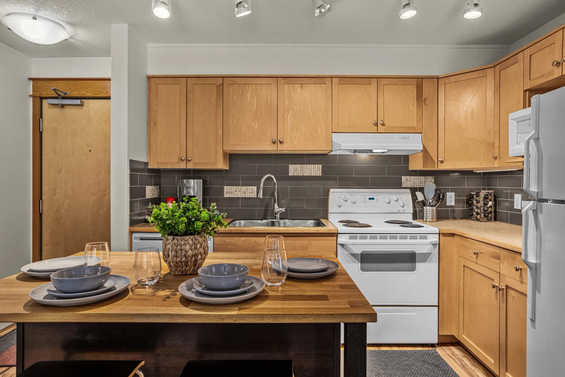 Kitchen with wood cabinets, white appliances and a dining table set with dishes.