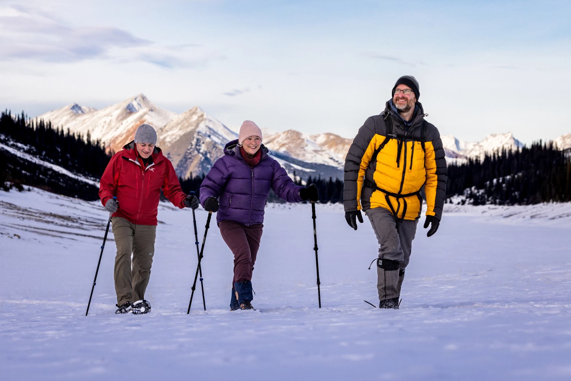 Three people snowshoeing in a snowy mountain landscape.
