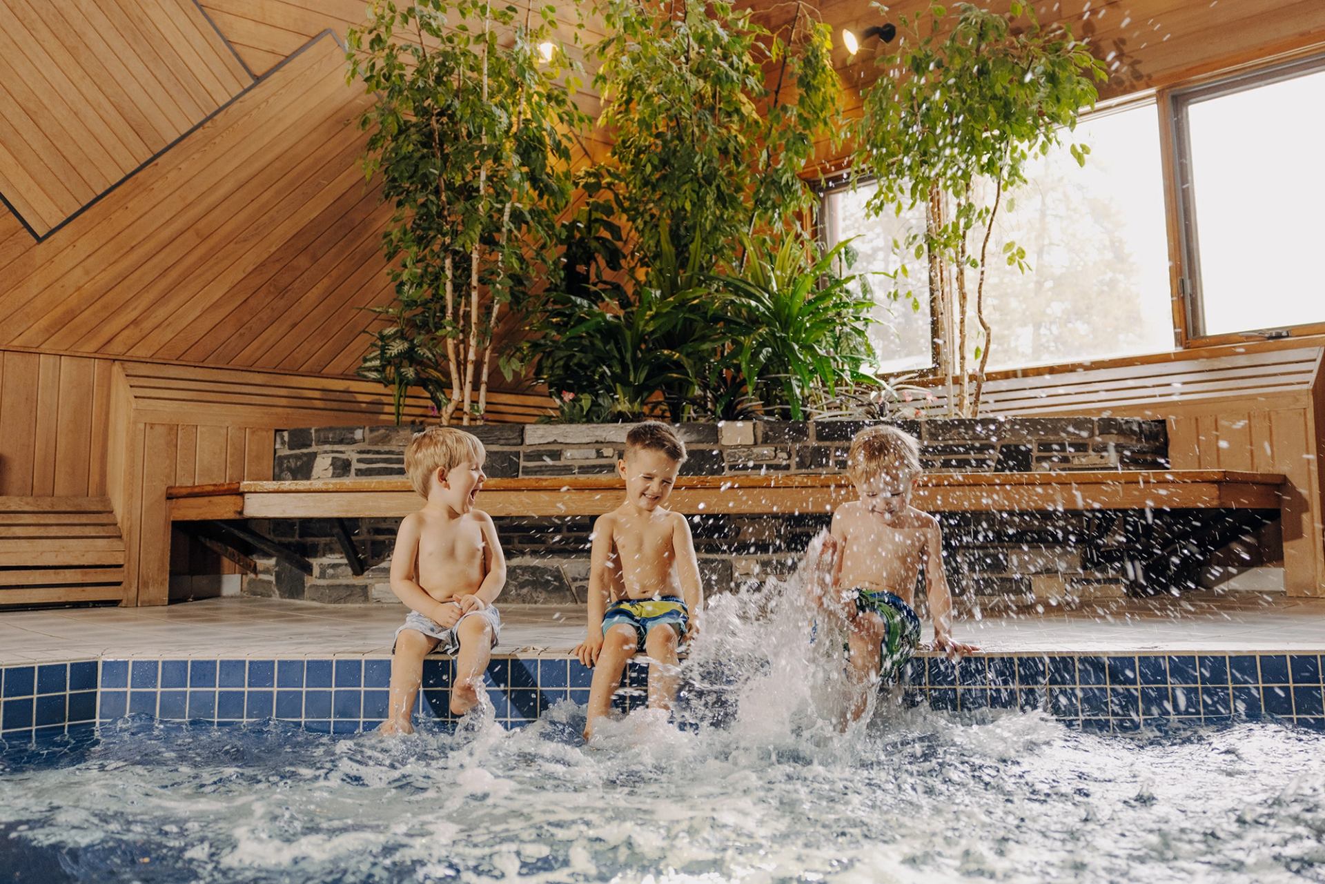 Kids splashing in indoor pool at Mountaineer Lodge with wood walls and plants.