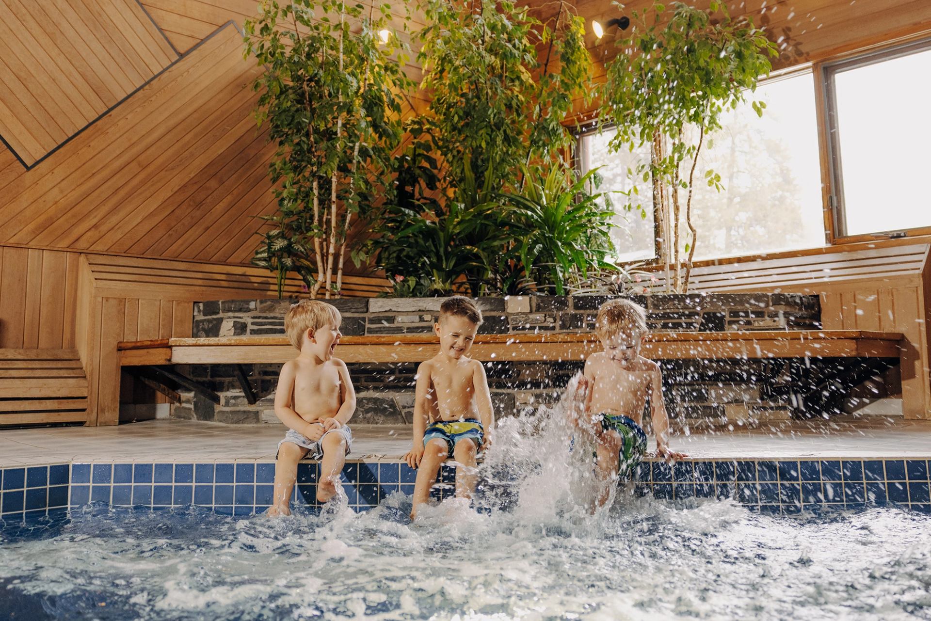 Kids splashing in indoor pool at Mountaineer Lodge with wood walls and plants.