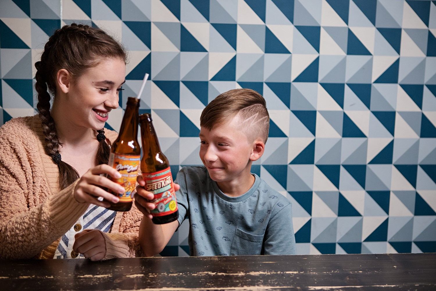 Two kids smile and clink bottles of craft soda during a food tour stop