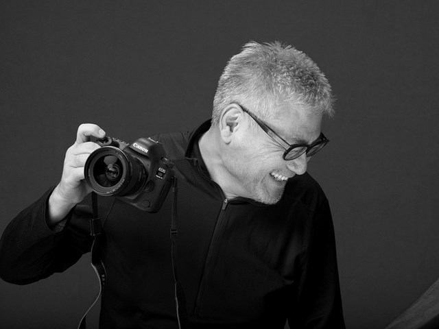 Photographer holds a camera with a lens in an indoor studio with plain backdrop.
