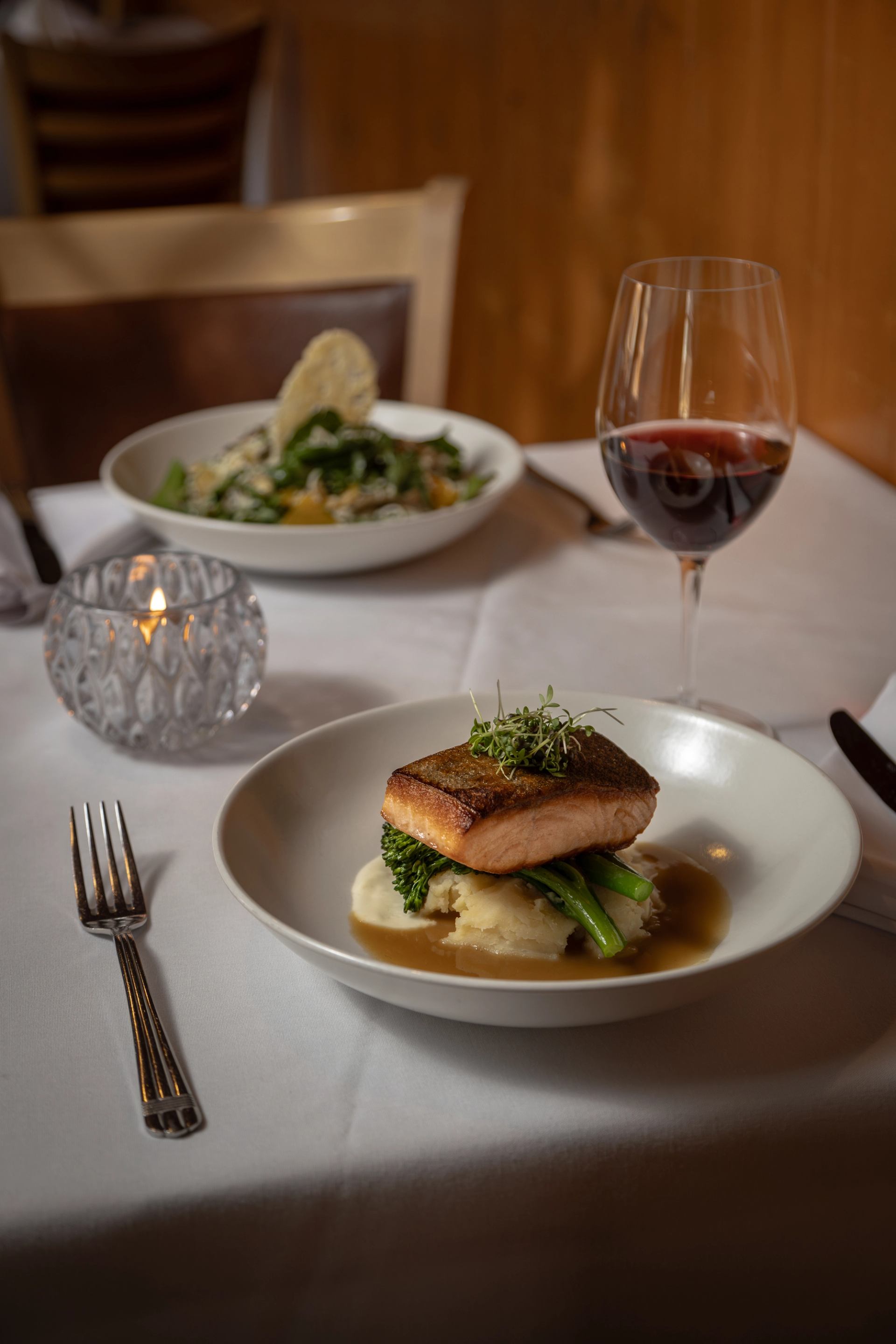 Plated salmon on mashed potatoes and broccolini with a glass of red wine.