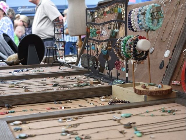 Handcrafted jewelry displayed on wooden trays at an outdoor market stall.