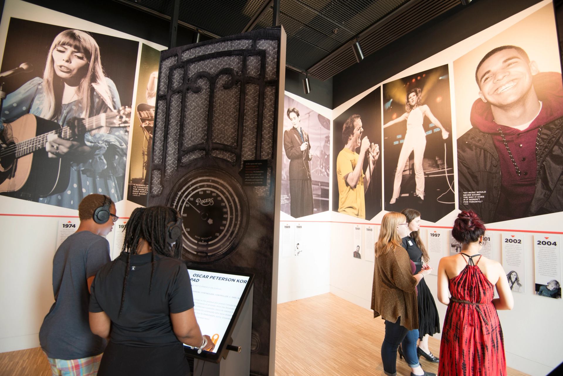 Visitors wearing headphones explore music exhibit with large musician portraits and interactive displays.