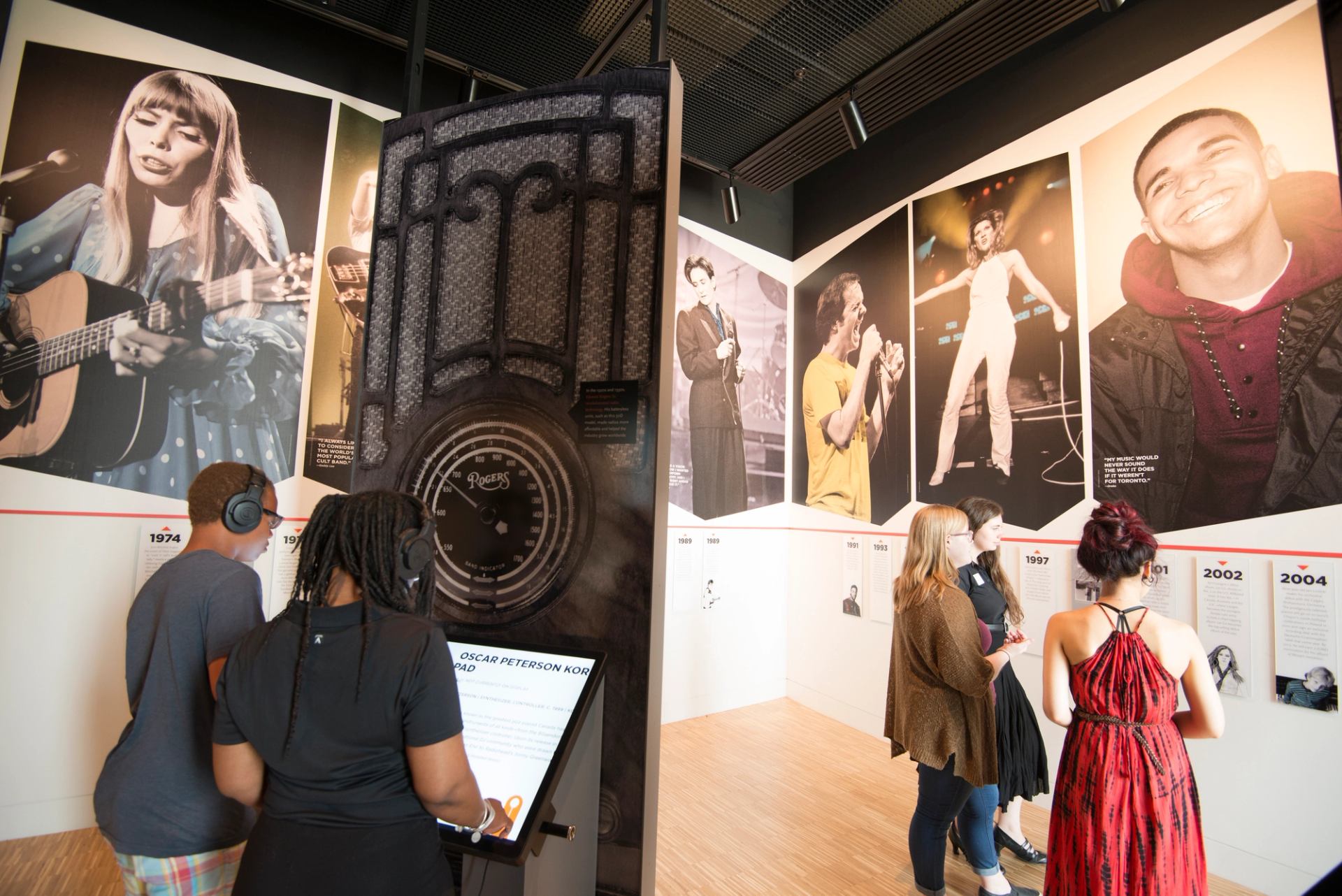 Visitors wearing headphones explore music exhibit with large musician portraits and interactive displays.