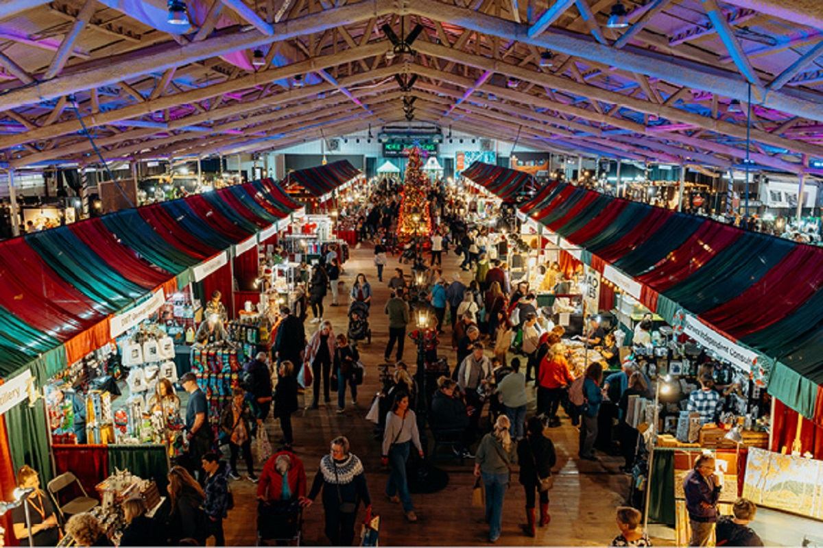 A large crowd of people visit red and green vendors booths.