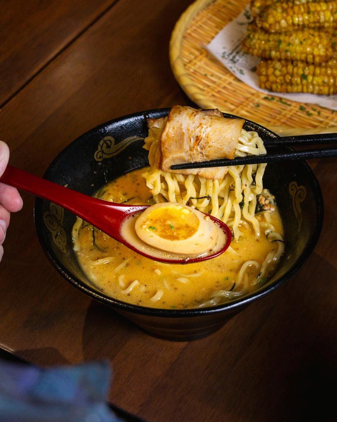 Bowl of ramen with pork, egg, noodles, and chopsticks on a red table setting.