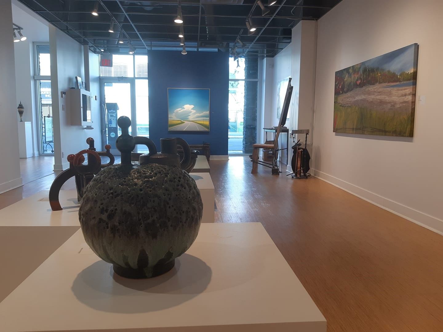 Art gallery interior with ceramic sculptures on plinths, landscape paintings and easel.