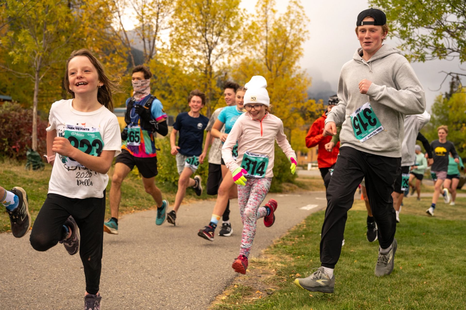 Group of runners with race bibs jogging on park path lined with yellow trees.