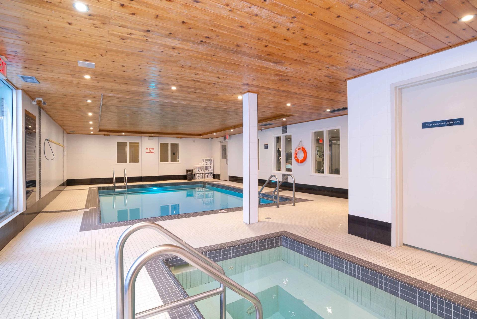 Indoor pool area with hot tub, tiled deck, wood ceiling and safety equipment.