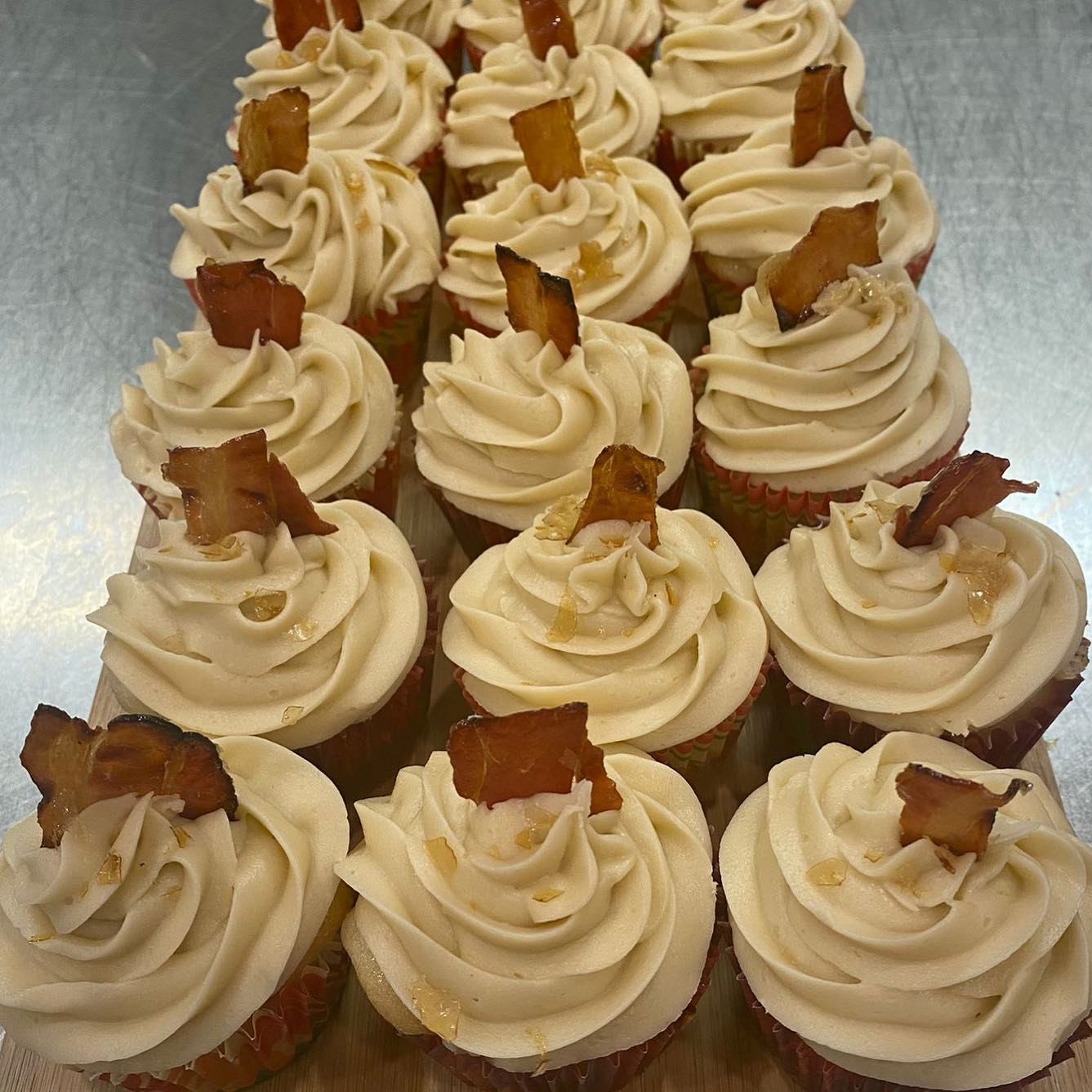 Frosted cupcakes topped with crispy bacon, arranged in neat rows on a tray.