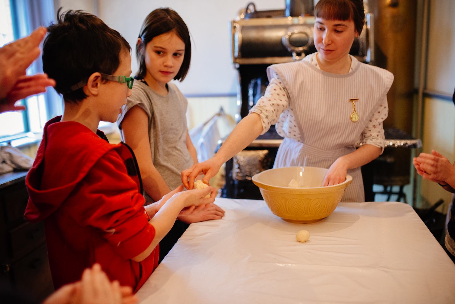 Instructor in apron helps children shape dough balls beside a large mixing bowl.