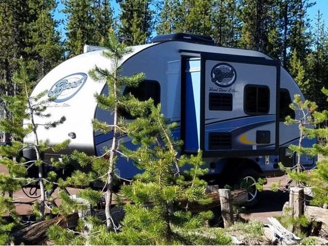 Compact RV trailer parked in forest with Rangeland RV logo on side.