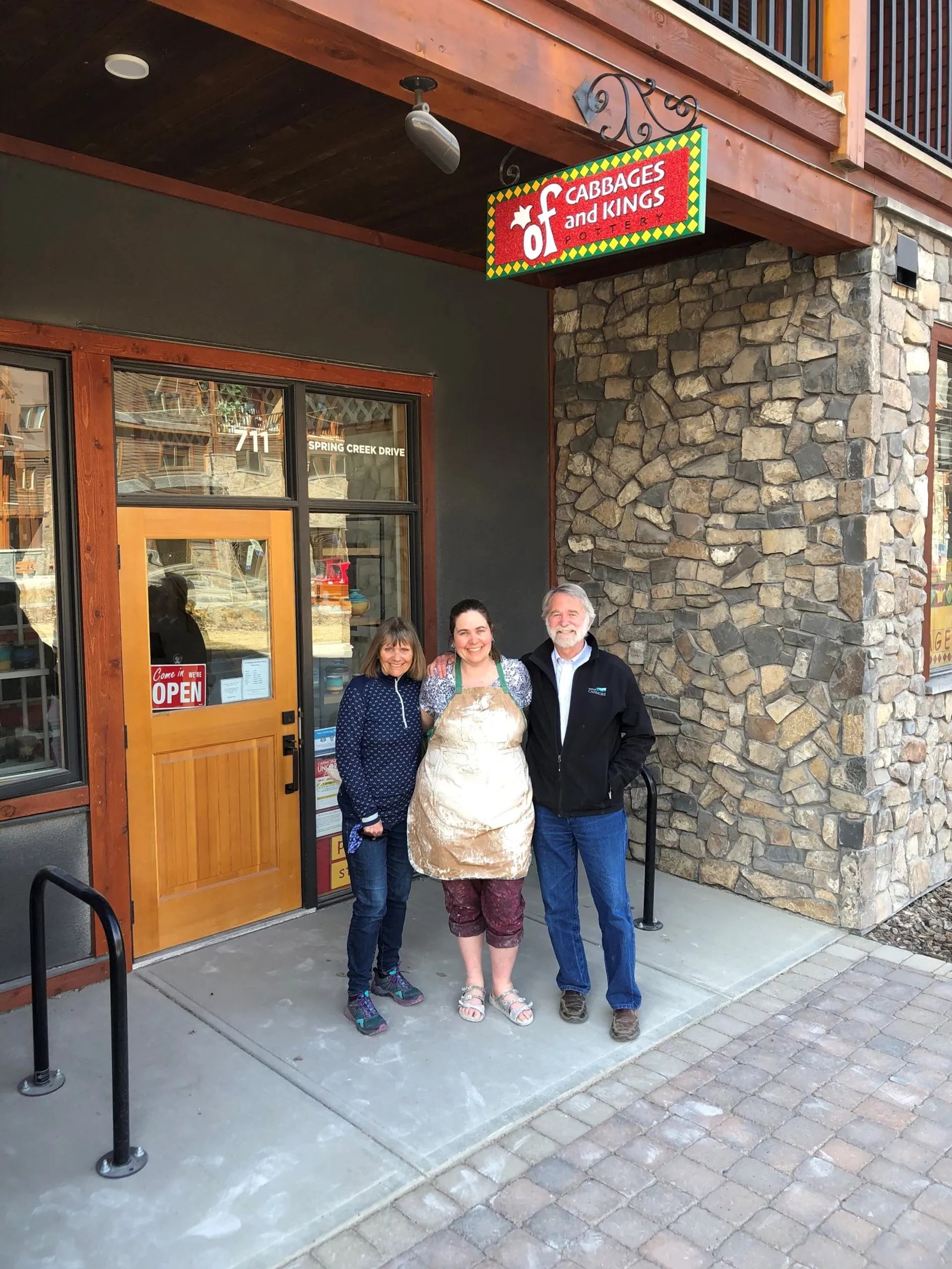 Three people stand outside Cabbages and Kings storefront with stone and wood exterior.