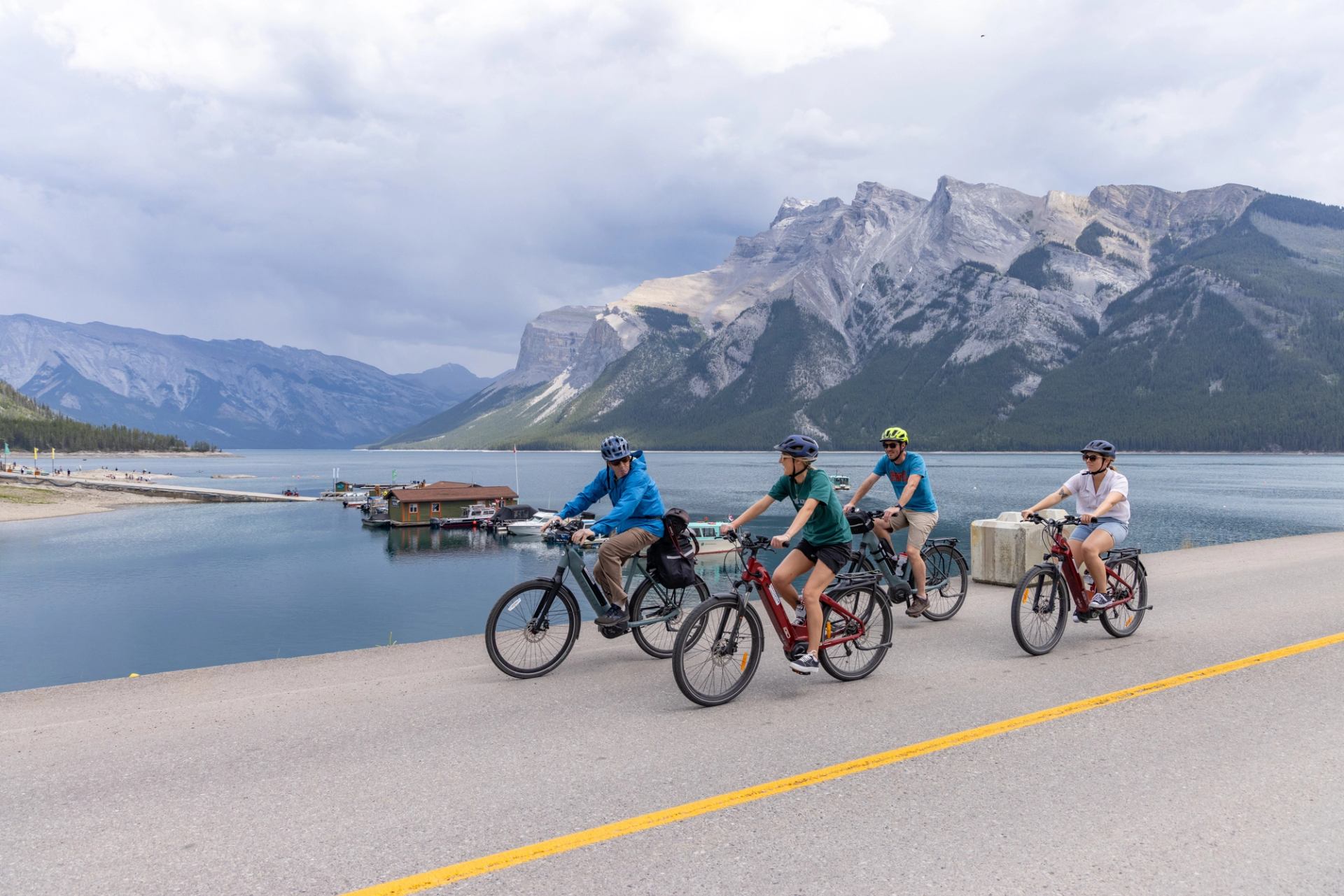 Four cyclists ride beside lake with mountain backdrop under clear skies in Banff.