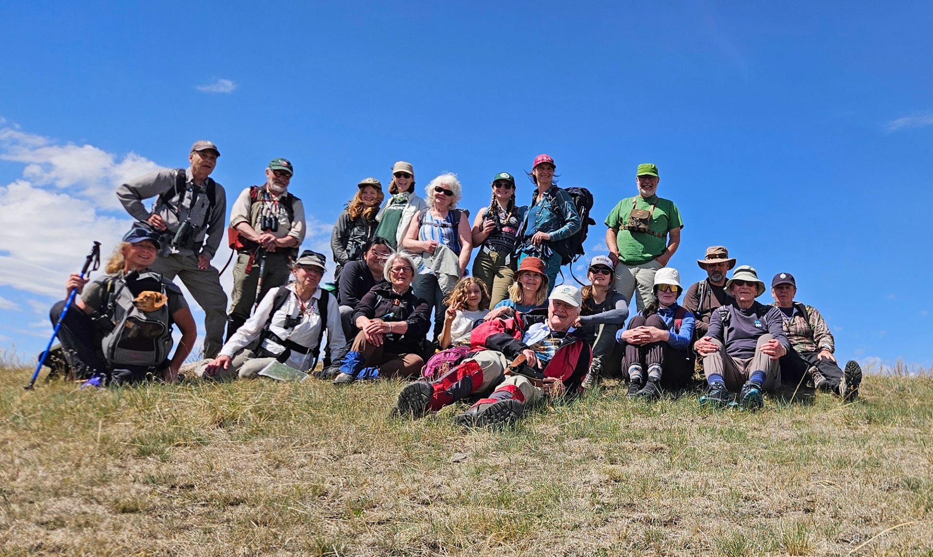 Group of hikers with backpacks resting on grassy hill under clear blue sky.
