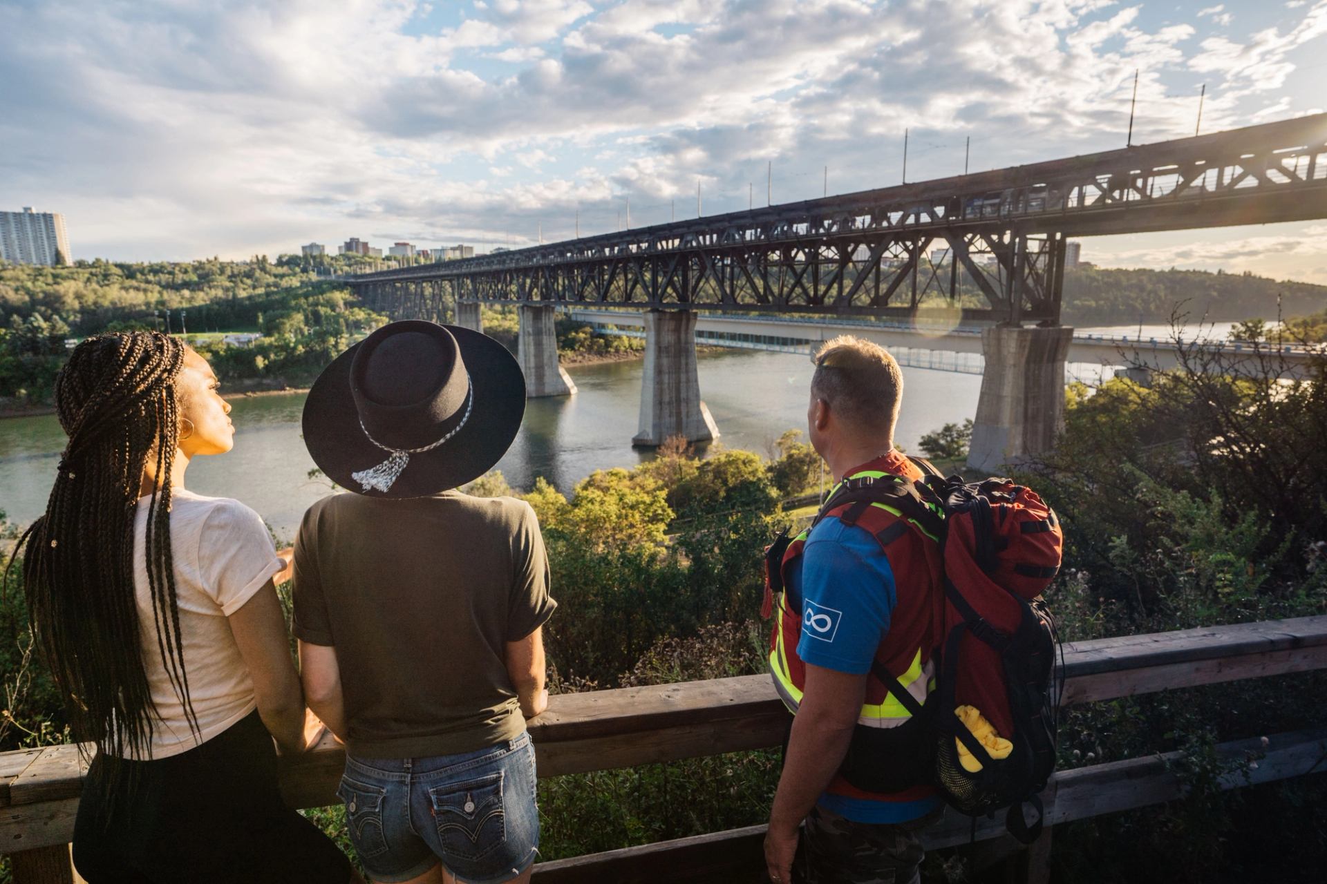 Three people view the Edmonton River Valley and the nearby High Level Bridge from a lookout.