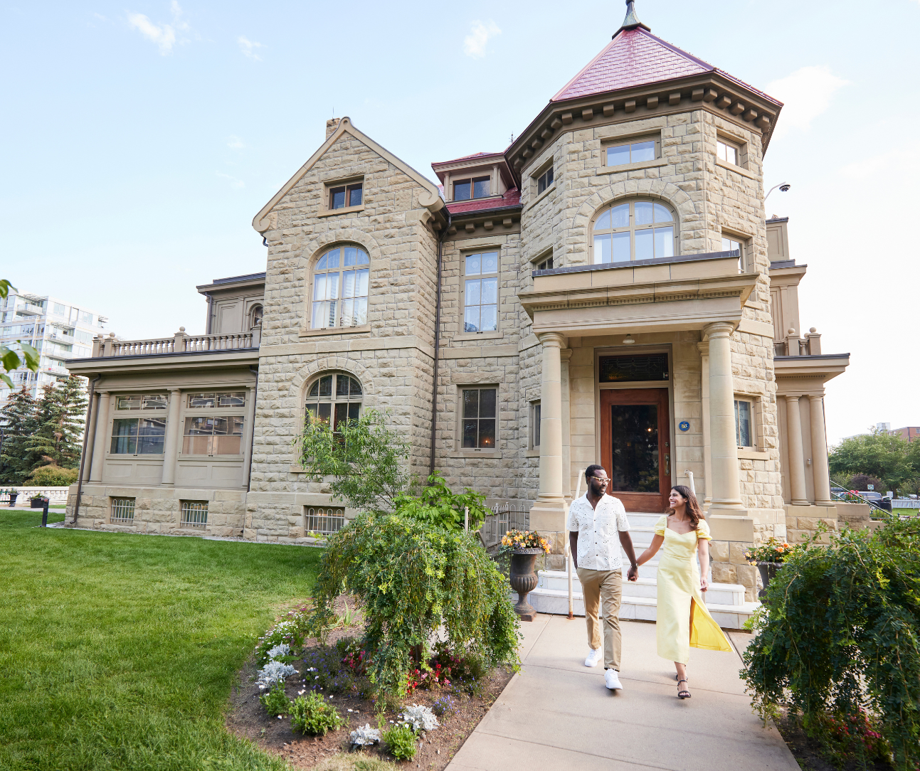 Historic stone building with red roof, garden, and visitors walking the path.