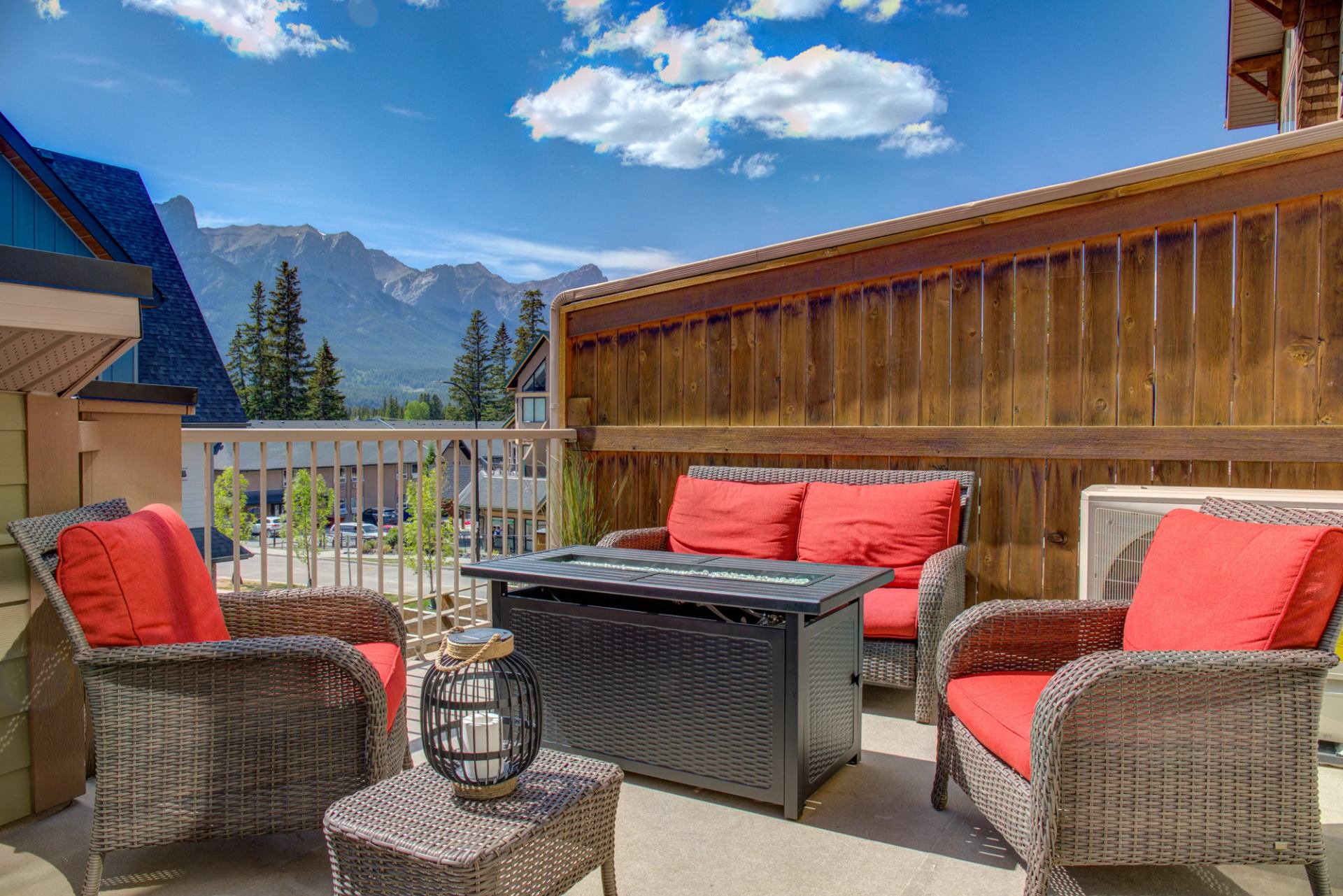 Outdoor patio with red cushioned chairs, fire table, and mountain views under a blue sky.