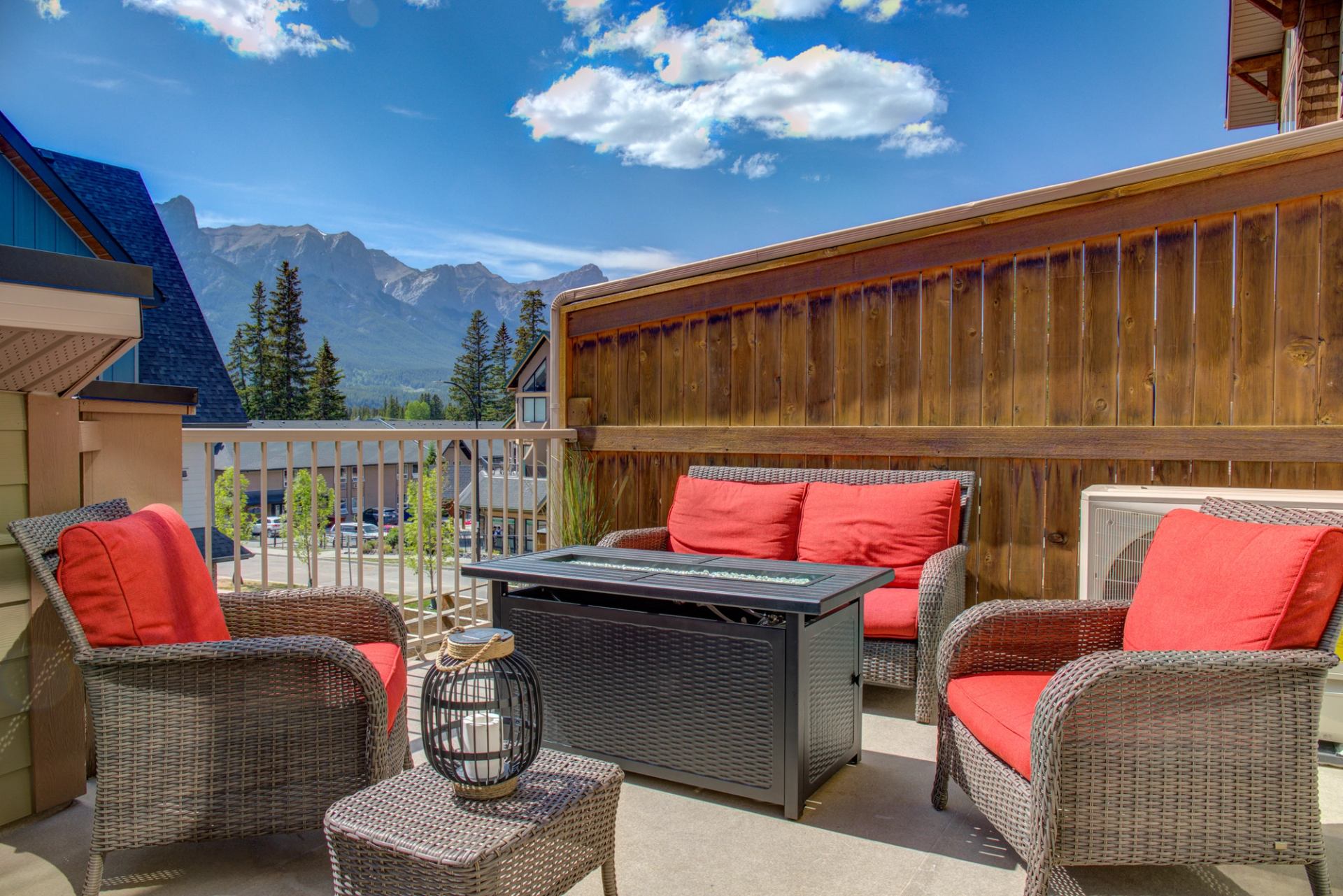 Outdoor patio with red cushioned chairs, fire table, and mountain views under a blue sky.