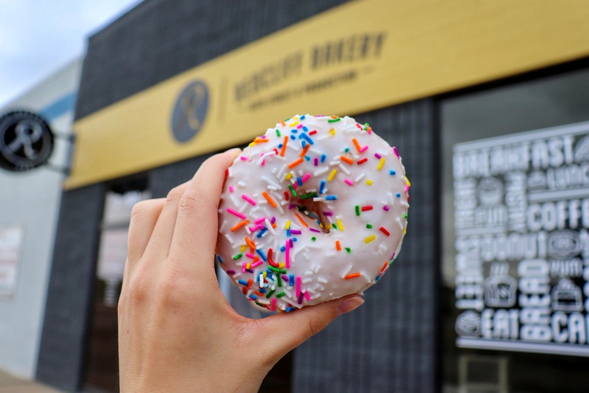 Hand holding sprinkled donut in front of Redcliff Bakery