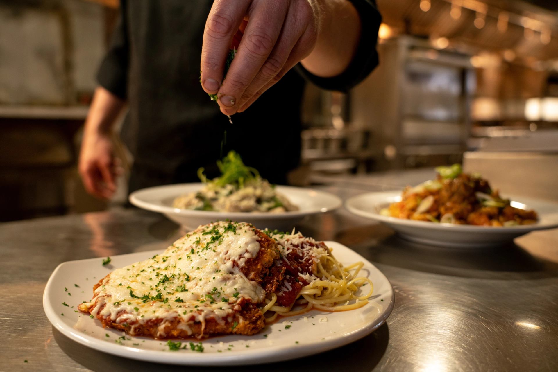 Chicken parmesan with spaghetti, garnished with herbs in a pro kitchen.