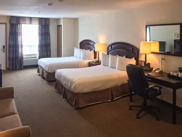 Hotel room with two beds, desk, armchair, and natural light from window.