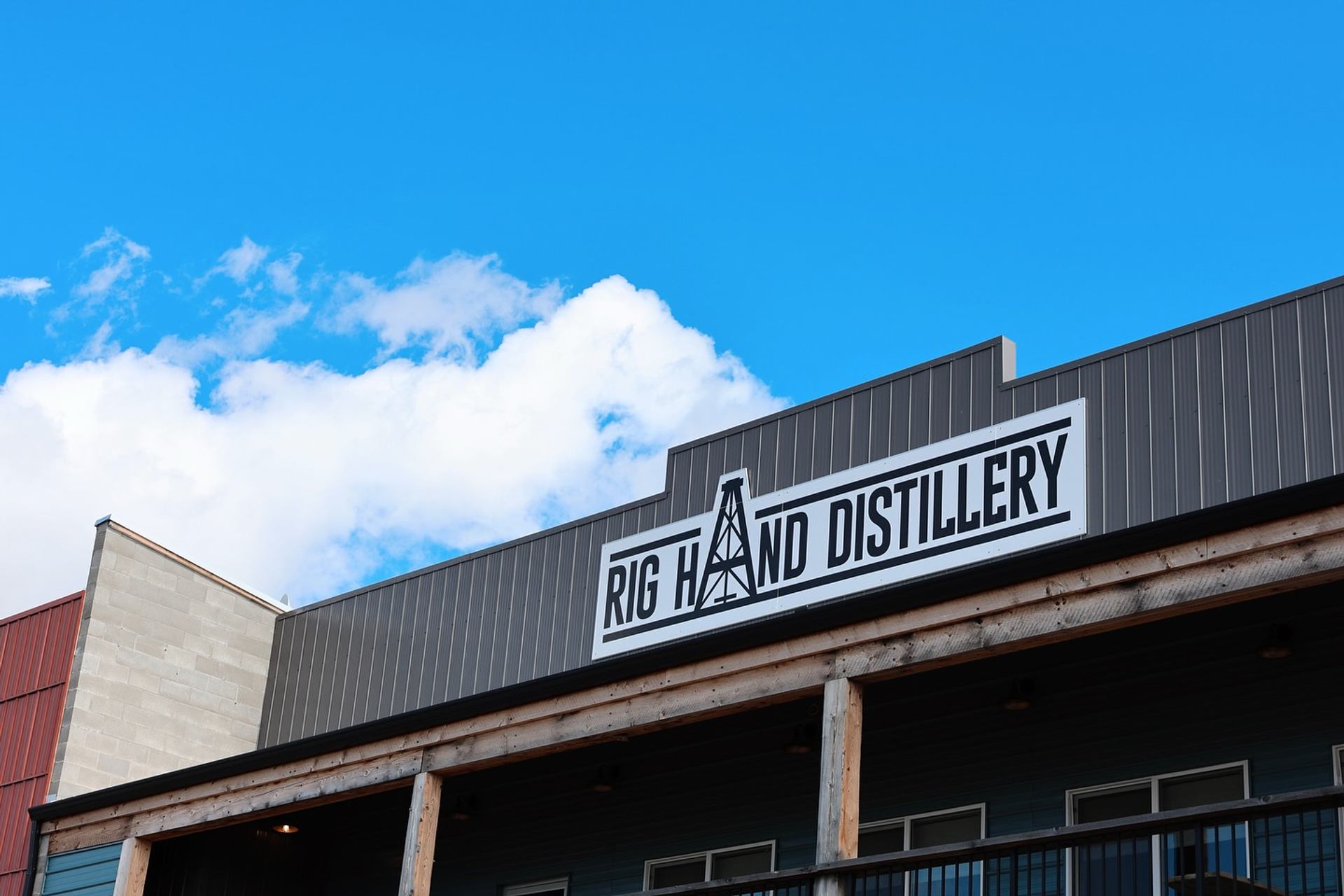 A distillery building stands beneath a bright blue sky with large white clouds overhead.