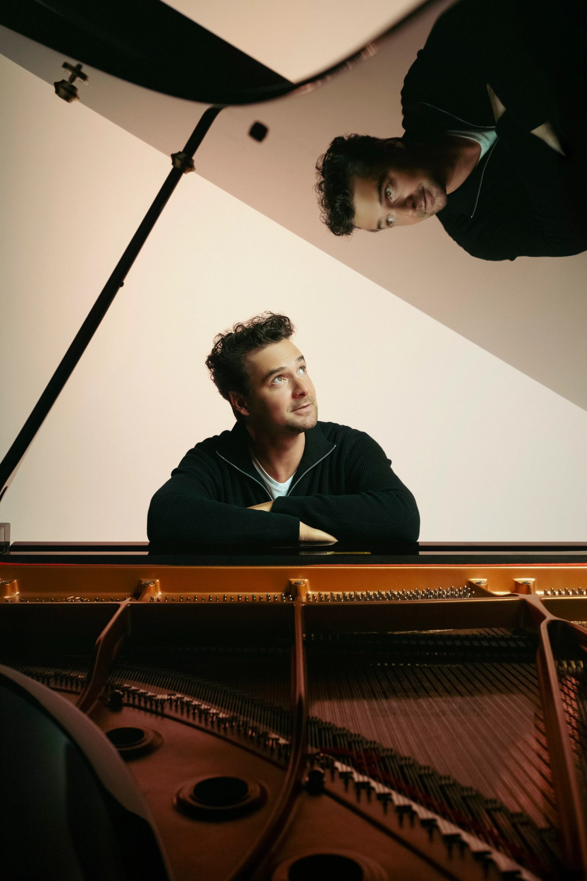 Person leaning on grand piano, looking upward, reflected in raised piano lid.