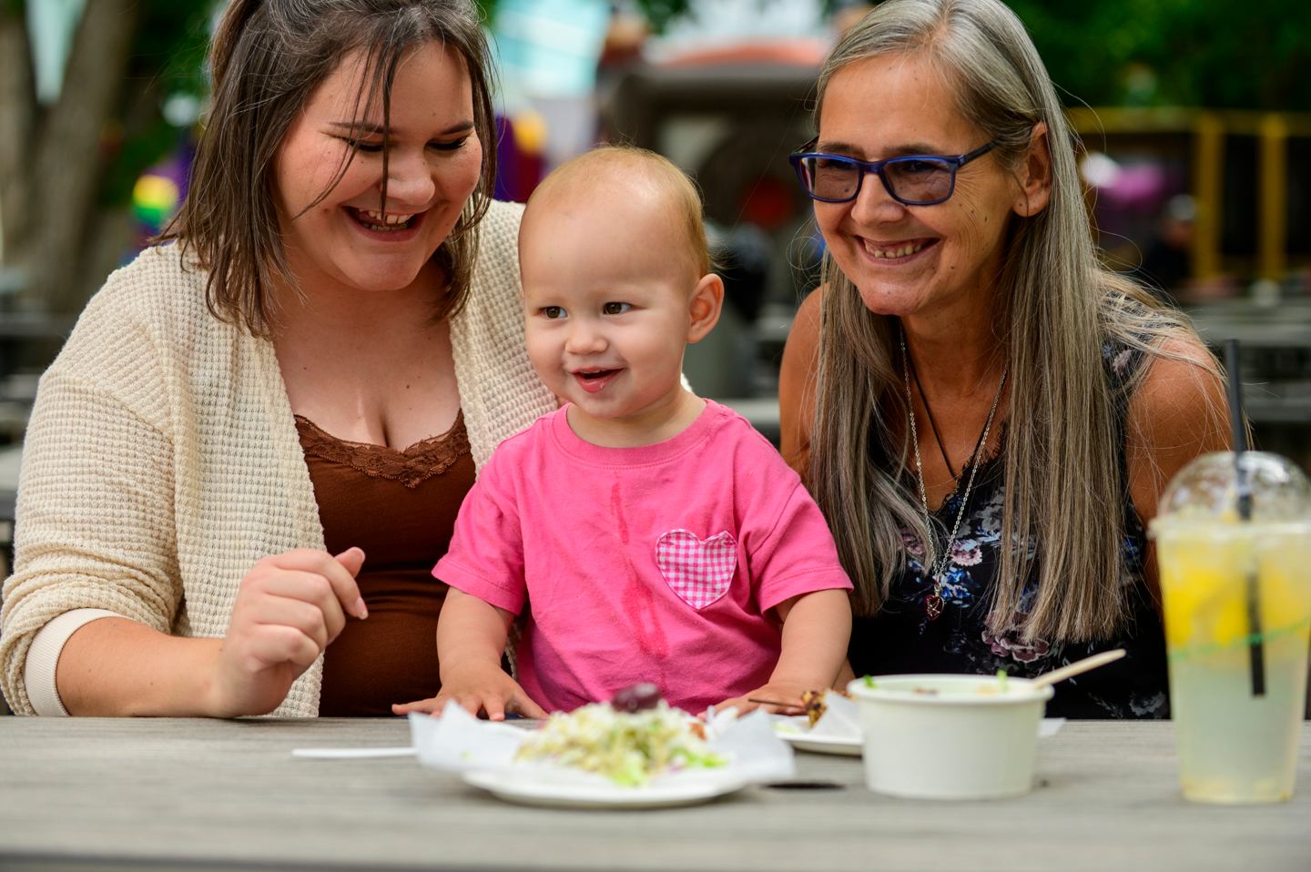Three people sitting at a picnic table with food and drinks.