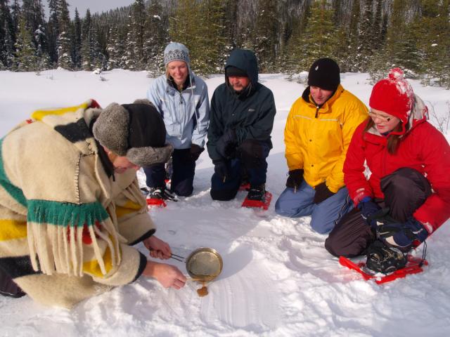 Tour guide pouring maple taffy on the snow for a group on a snowshoeing tour of Marble Canyon in Banff National Park.