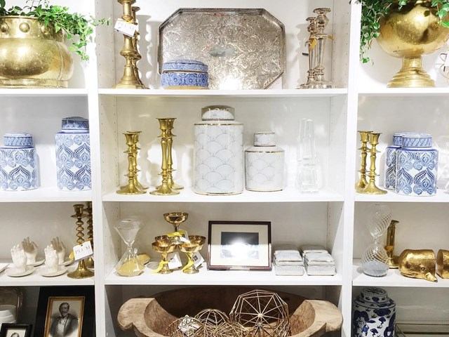 Antique shop shelf with brass candlesticks, porcelain vases, and decorative boxes in Edmonton store .