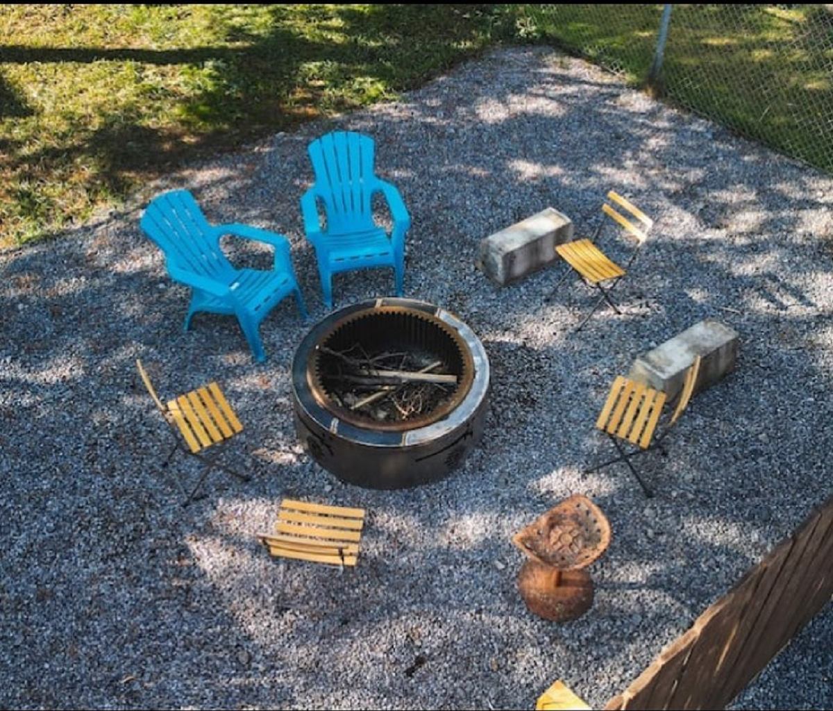 Outdoor firepit surrounded by blue chairs and small wooden seats on a gravel patio.