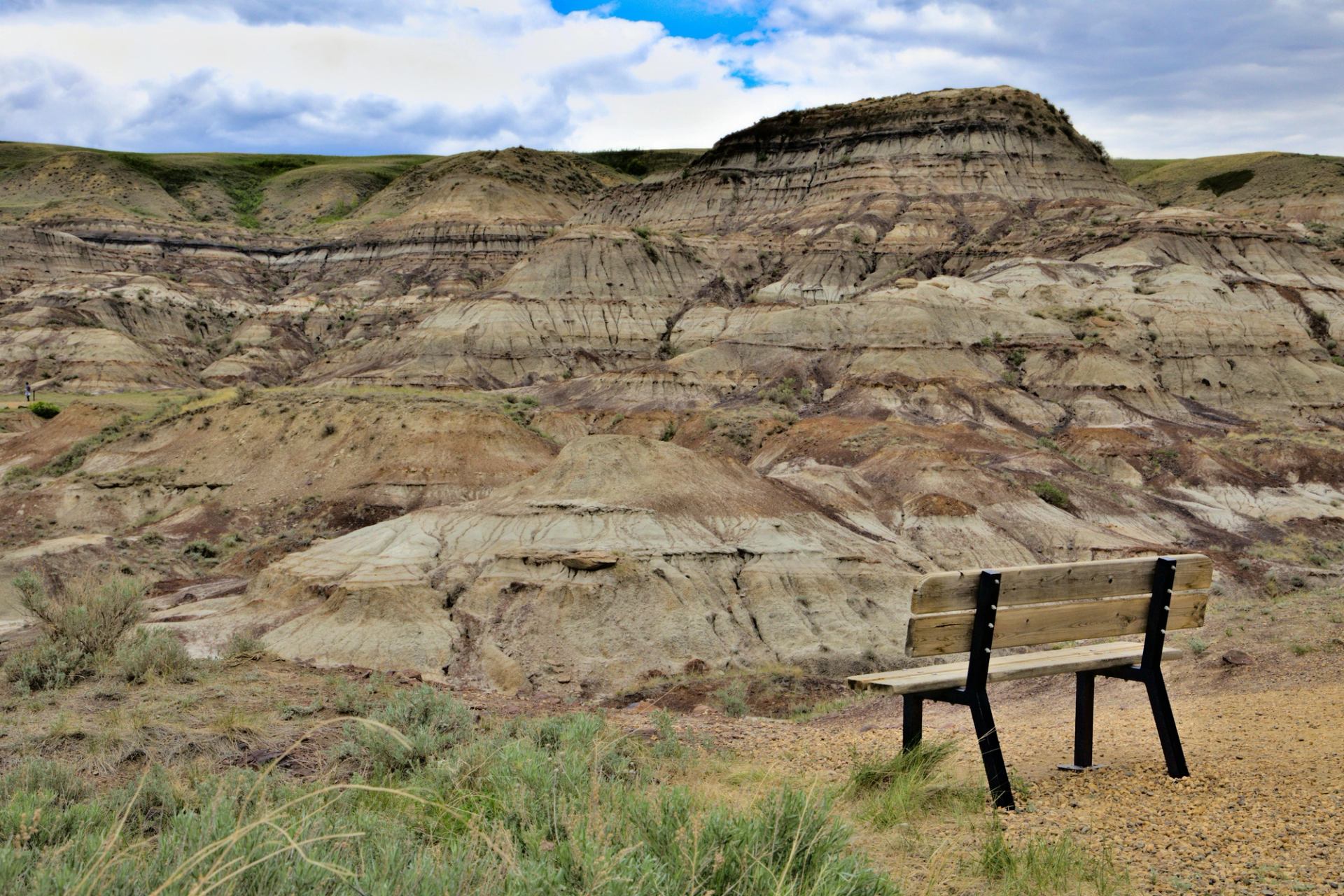 Wooden bench overlooks layered badlands hills under a cloudy blue and white sky.