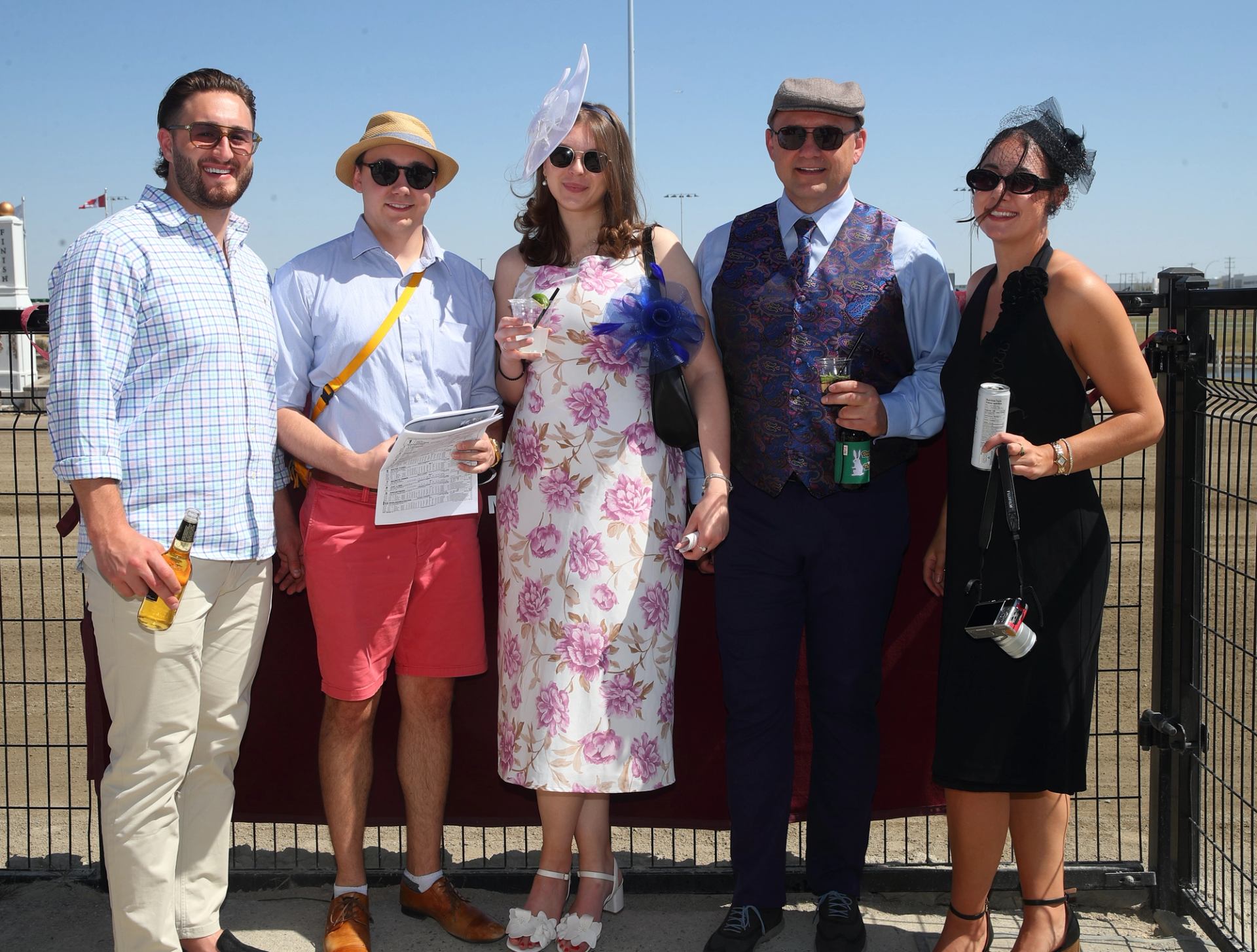 Group in formal derby attire posing near race track fence