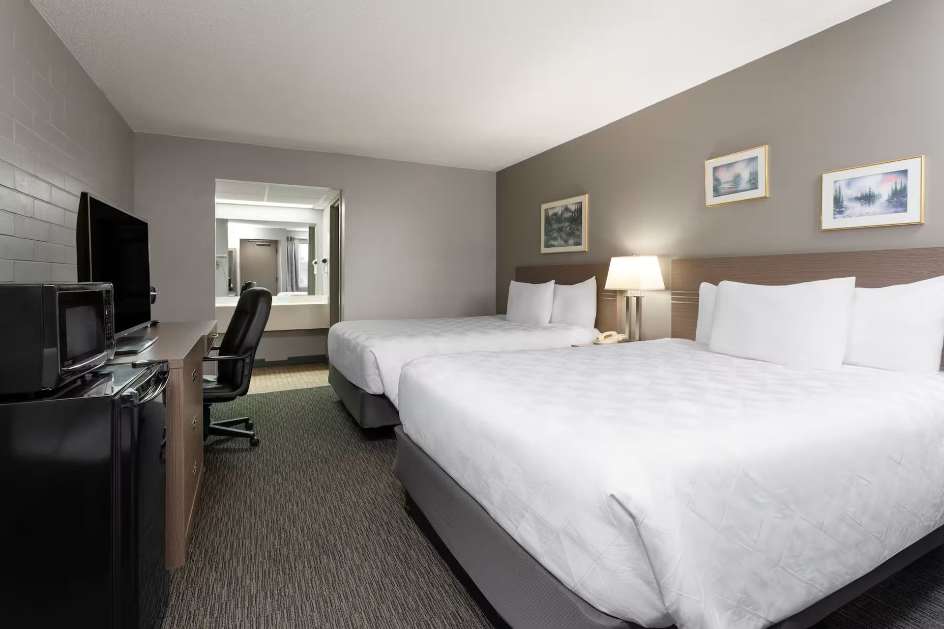 Hotel room with two beds, desk, TV, and mini-fridge at Travelodge Grande Prairie.