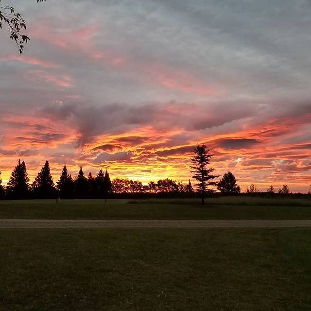 Fiery sunset over Spirit Creek Golf & Country Club with silhouetted trees.