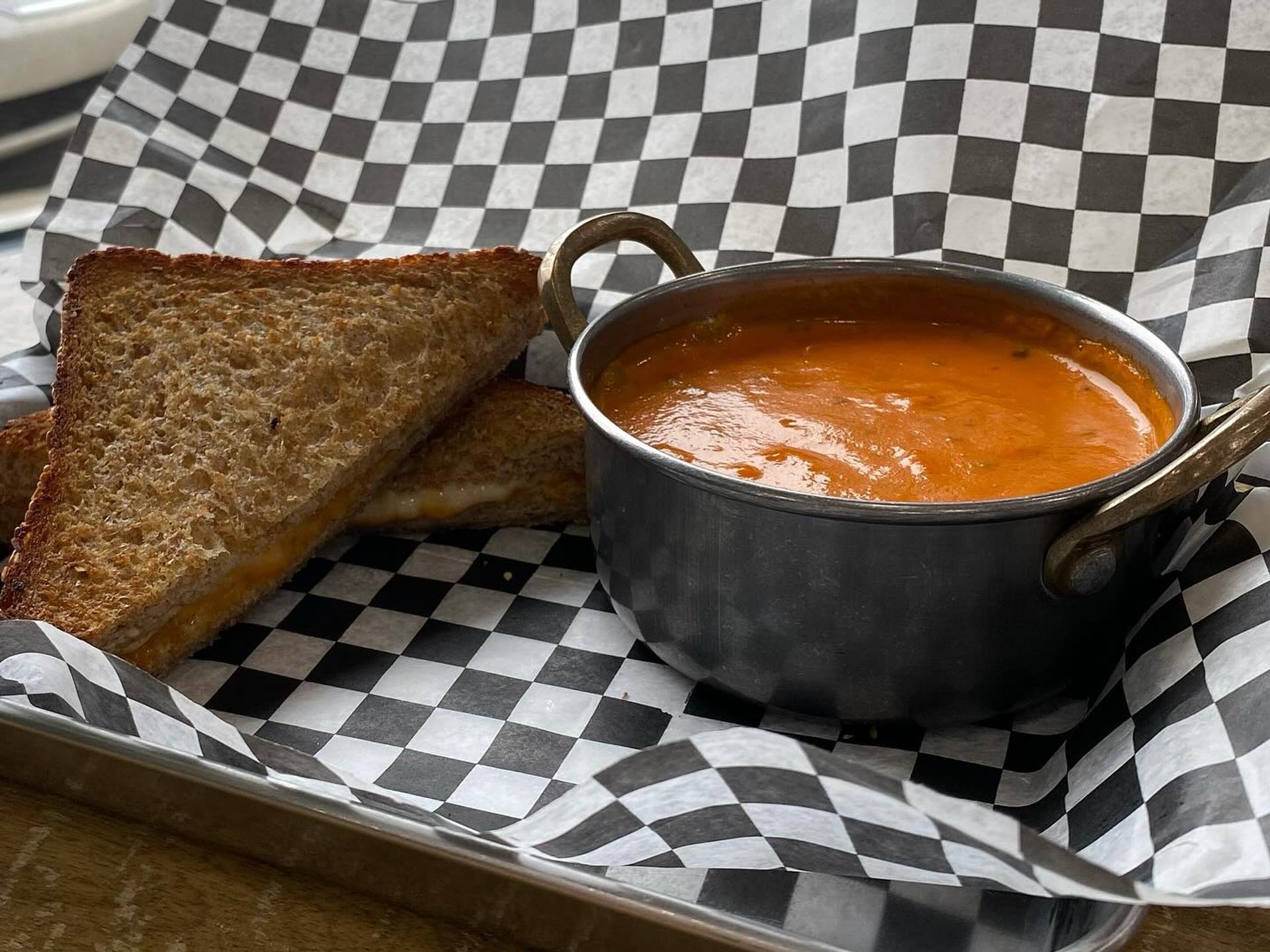 Tomato Bisque and grilled cheese served on a metal tray with checkered liner.