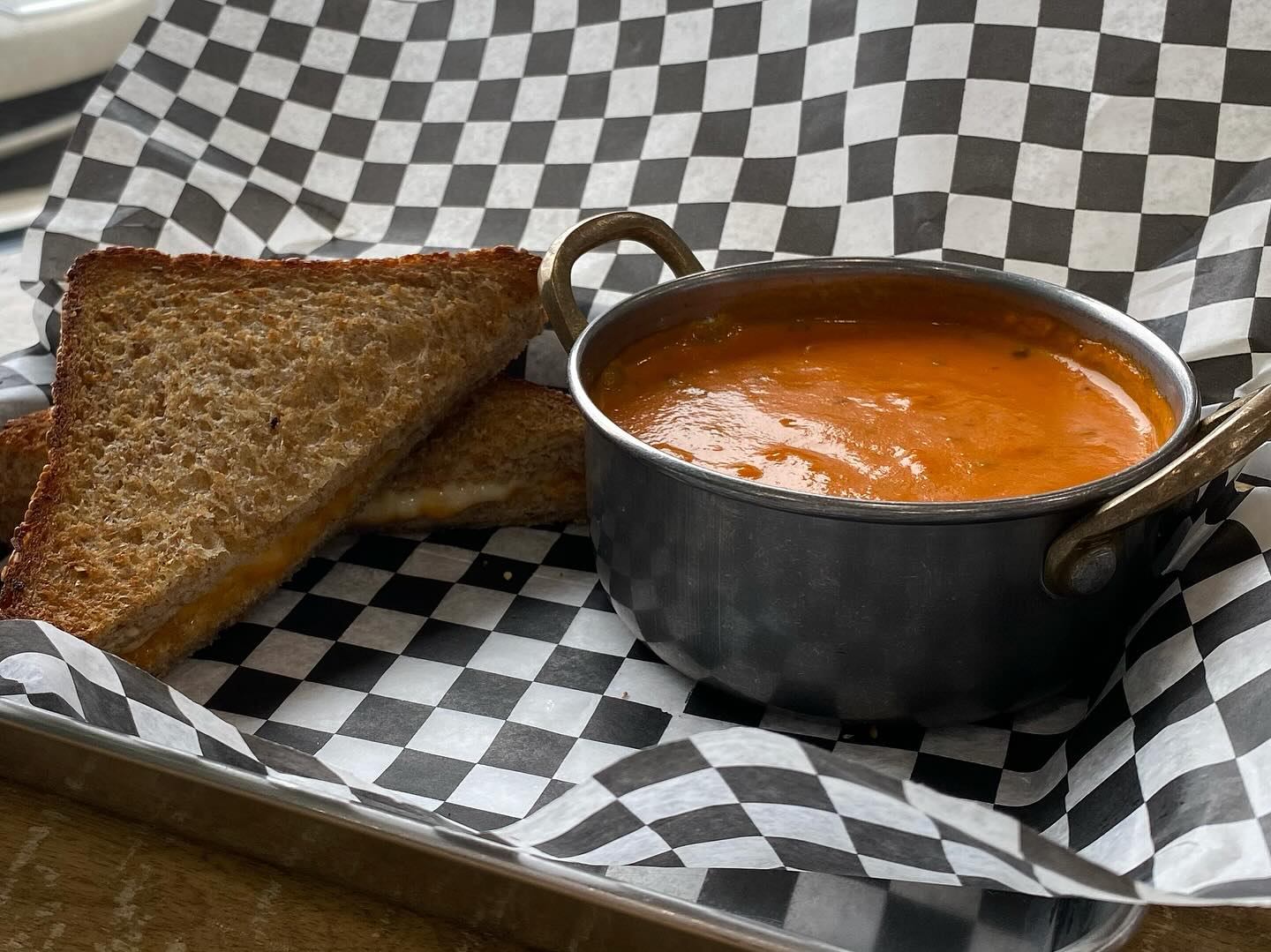 Tomato Bisque and grilled cheese served on a metal tray with checkered liner.