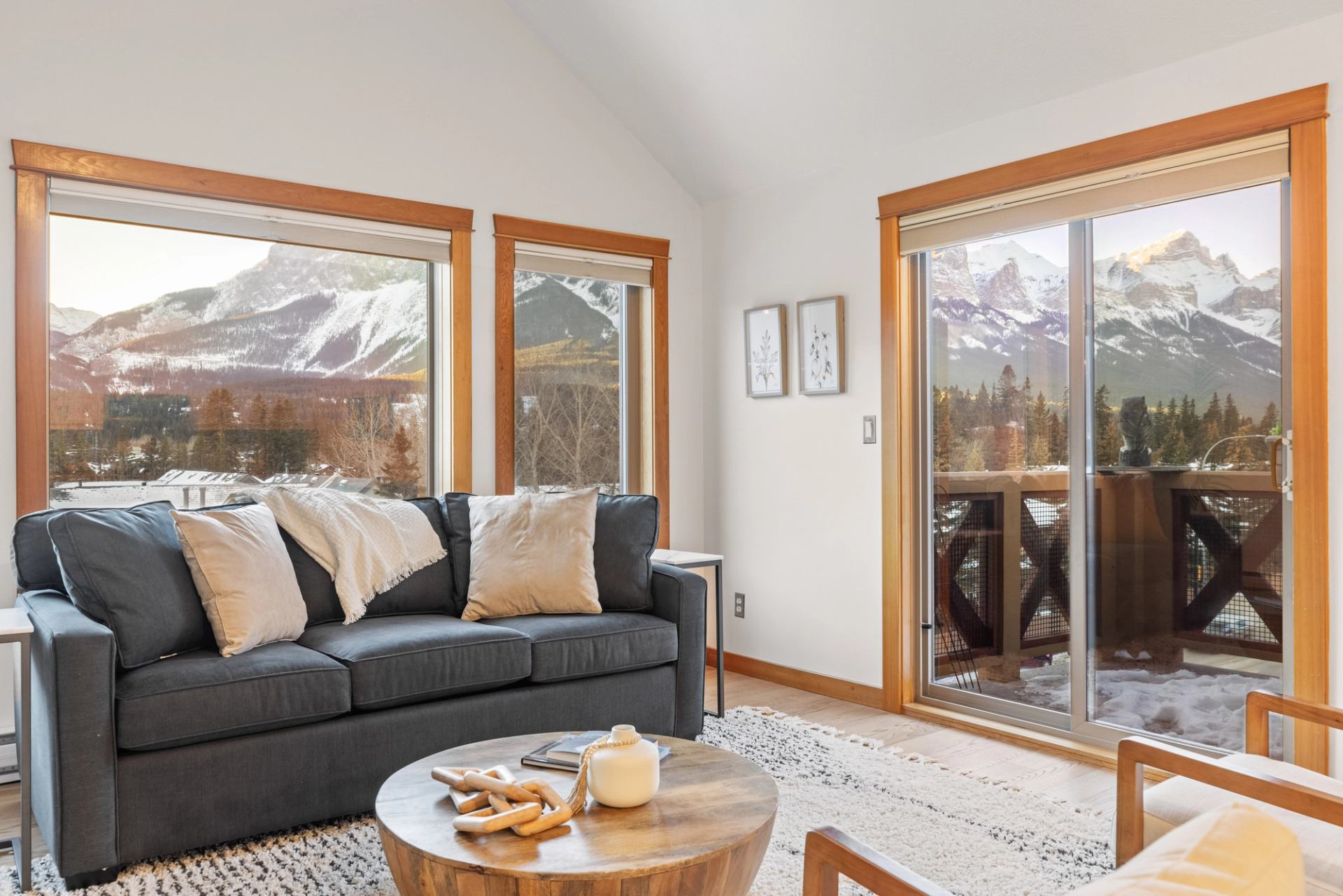 Living room with dark sofa and balcony, overlooking snow-covered mountain landscape through windows.
