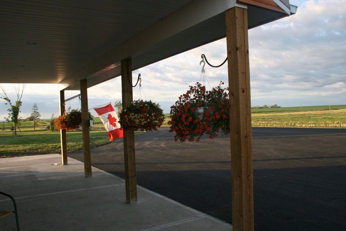 Covered porch at Happy Trails Campground with Canadian flag and hanging flower baskets.