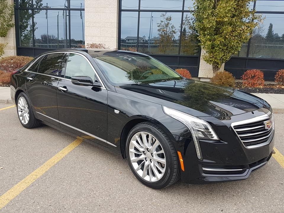 Black Cadillac sedan parked near a building by MC Limousine.